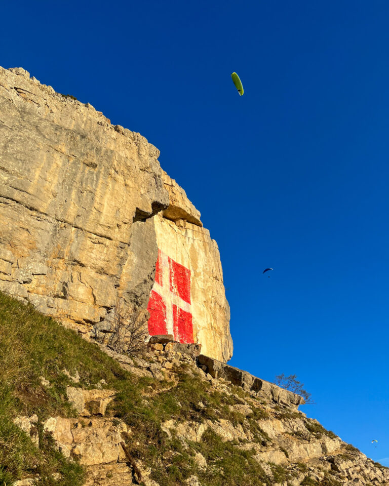 La croix de Savoie peinte sur la falaise du Salève, parapentes dans le ciel